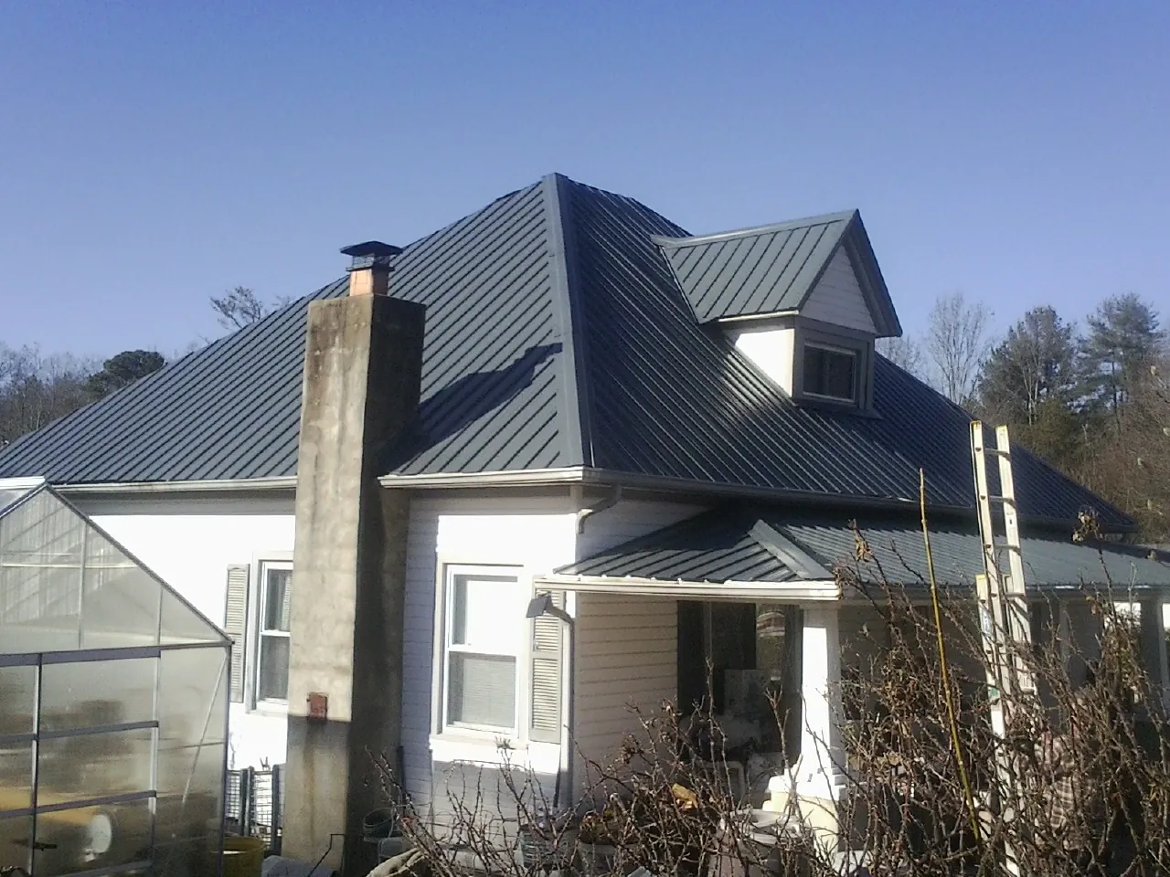 Dark blue standing seam metal roof on a white farmhouse with dormer — Slate & Tile Roof Repair by Roofing Brothers in Brownsboro