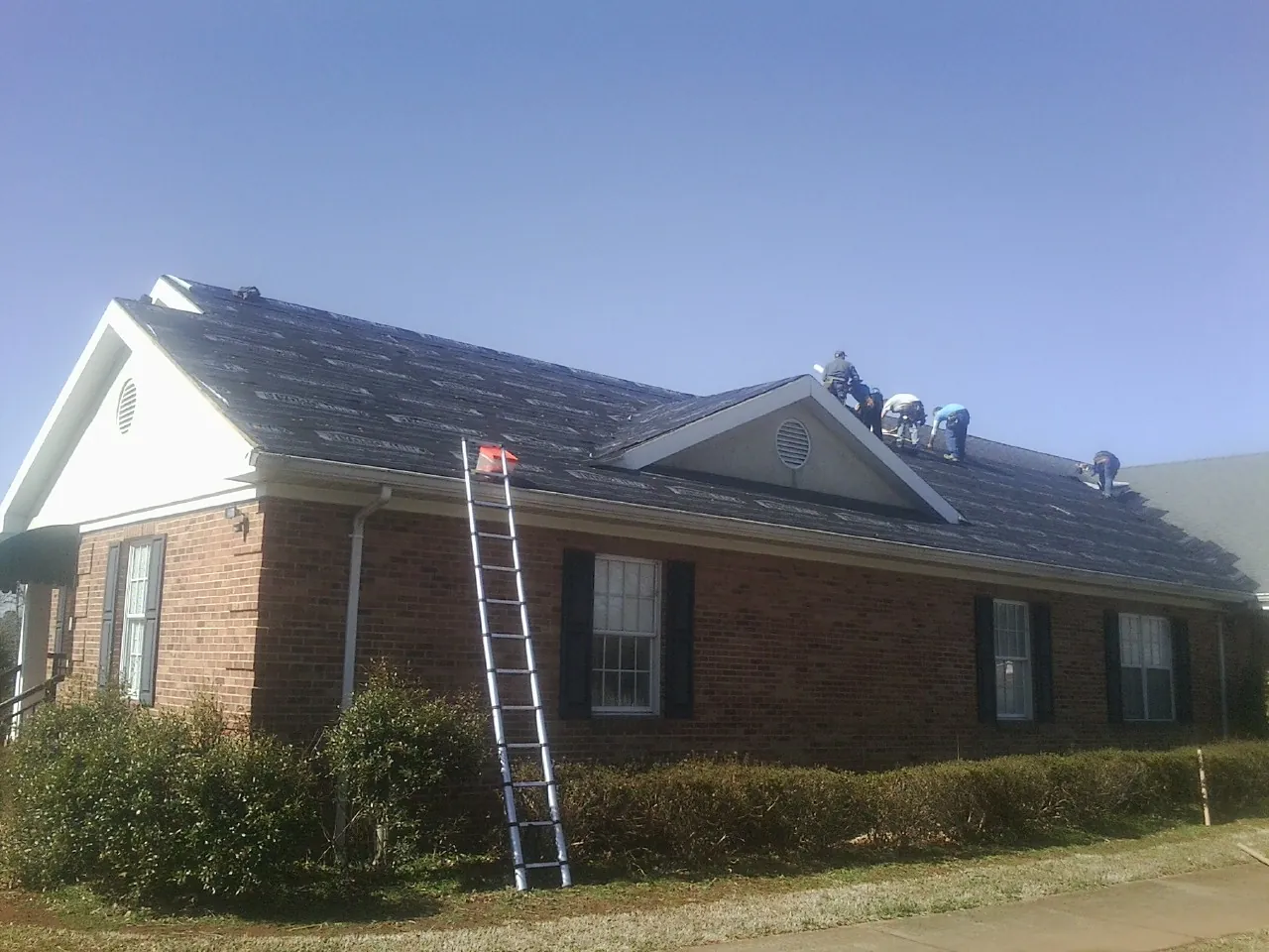 Crew tearing shingles off a brick ranch roof with a ladder set — Emergency Roof Repair work by our crew in Brownsboro