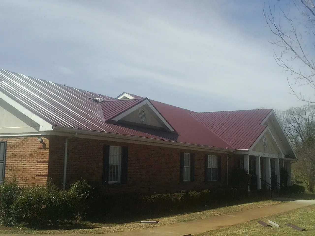 Red metal roof with gabled entries on a long brick building, from a Hail Damage Roof Repair job in Brownsboro
