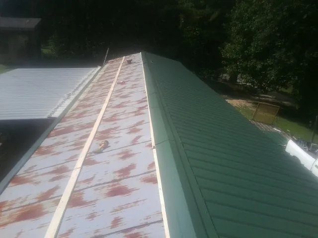 Old rusted panels beside newly installed green metal roofing — Wind Damage Roof Repair by Roofing Brothers in Brownsboro