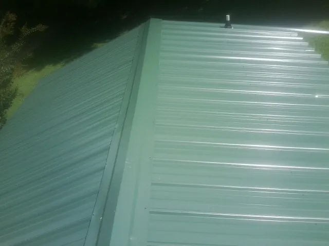 New green metal panels meeting at the ridge of a roof — Flat Roof Repair work by our crew in Brownsboro