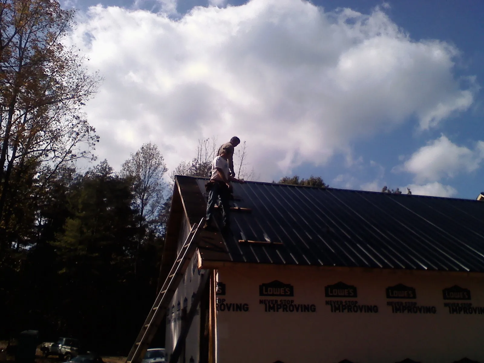 Roofer fastening dark metal panels high against a cloudy sky, from a Roof Inspection job in Brownsboro