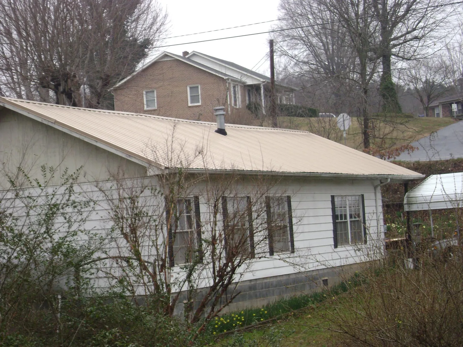 Tan metal roof on a white sided house set into a hillside — Commercial Roofing by Roofing Brothers in Brownsboro